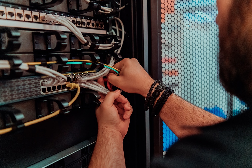 Netzwerktechniker arbeitet an einem Serverschrank und verbindet Netzwerkkabel